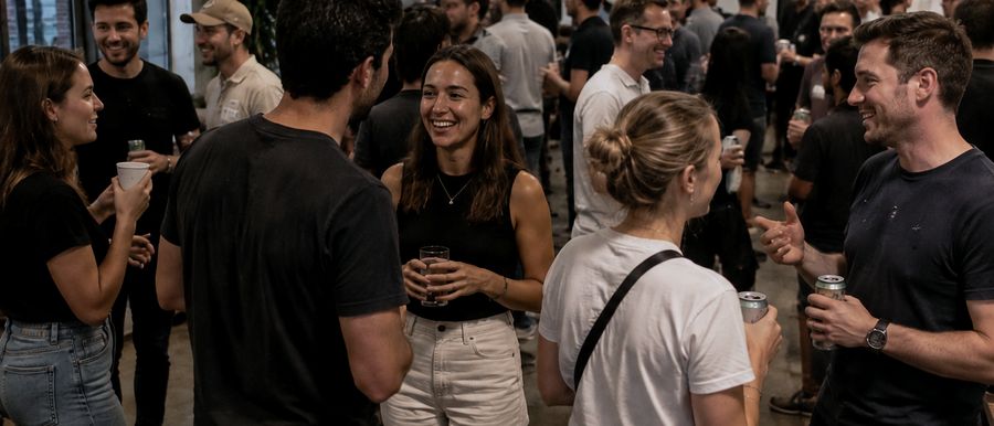 People talking in small groups at a gathering, drinks in hand.